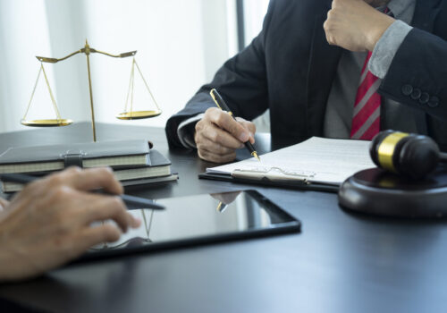 The lawyer is reviewing the draft of legal documents or contracts for clients near the staff or the client is checking work together by using a tablet.